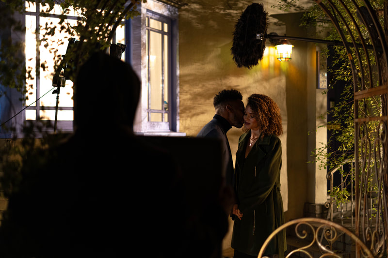 Samantha Neyland Trumbo in a still frame from movie Sinister Surgeon with actor Anthony Montgomery. Anthony Montgomery is leaning over to give the actress a kiss on the cheek as they stand on the front steps of a house.