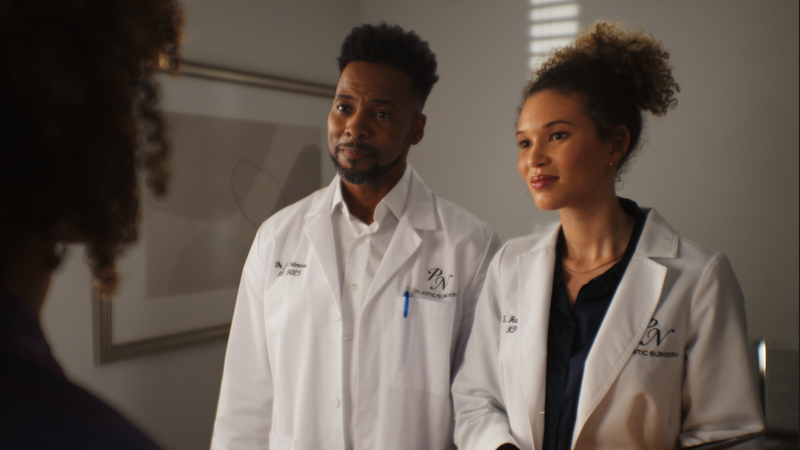 Samantha Neyland Trumbo in a still frame from movie Sinister Surgeon with actor Anthony Montgomery. The two actors are wearing white lab coats and looking at a patient off-screen.